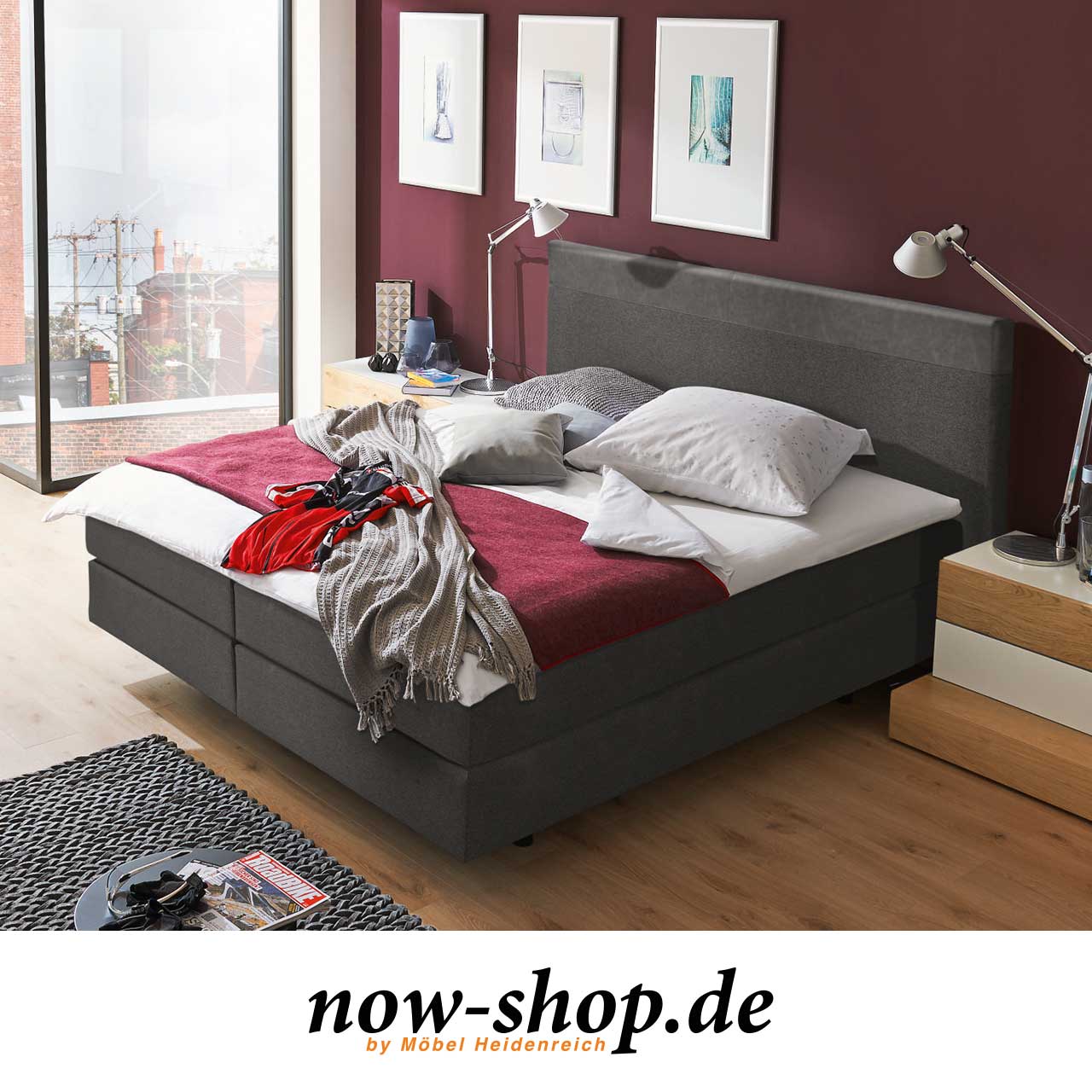 Boxspringbett aus anthrazitfarbenem Stoff mit Kunstleder-Applikation am Kopfteil. Milieuaufnahme Schlafzimmer.